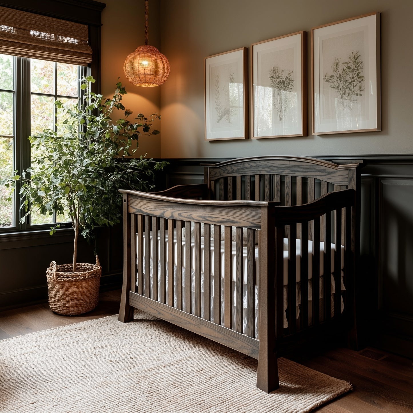 A cozy nursery with The Archer Crib in dark wood, a woven rug, a large potted plant, three botanical prints on the wall, a wicker pendant light, and sunlight streaming through window blinds.