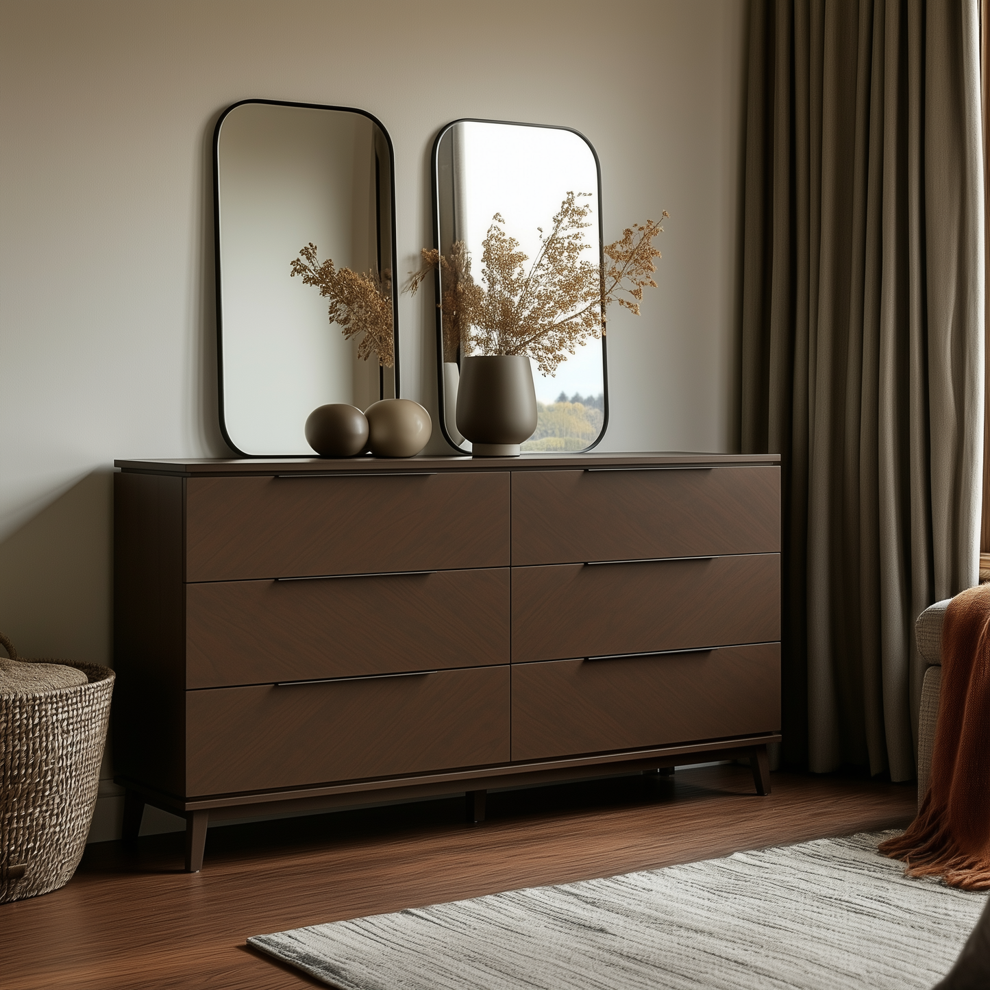 A modern bedroom setup featuring The Adelaide 6-Drawer Dresser in dark wood, two vases with dried plants, rectangular mirrors, a woven basket, beige curtains, and a striped rug on wooden floors.