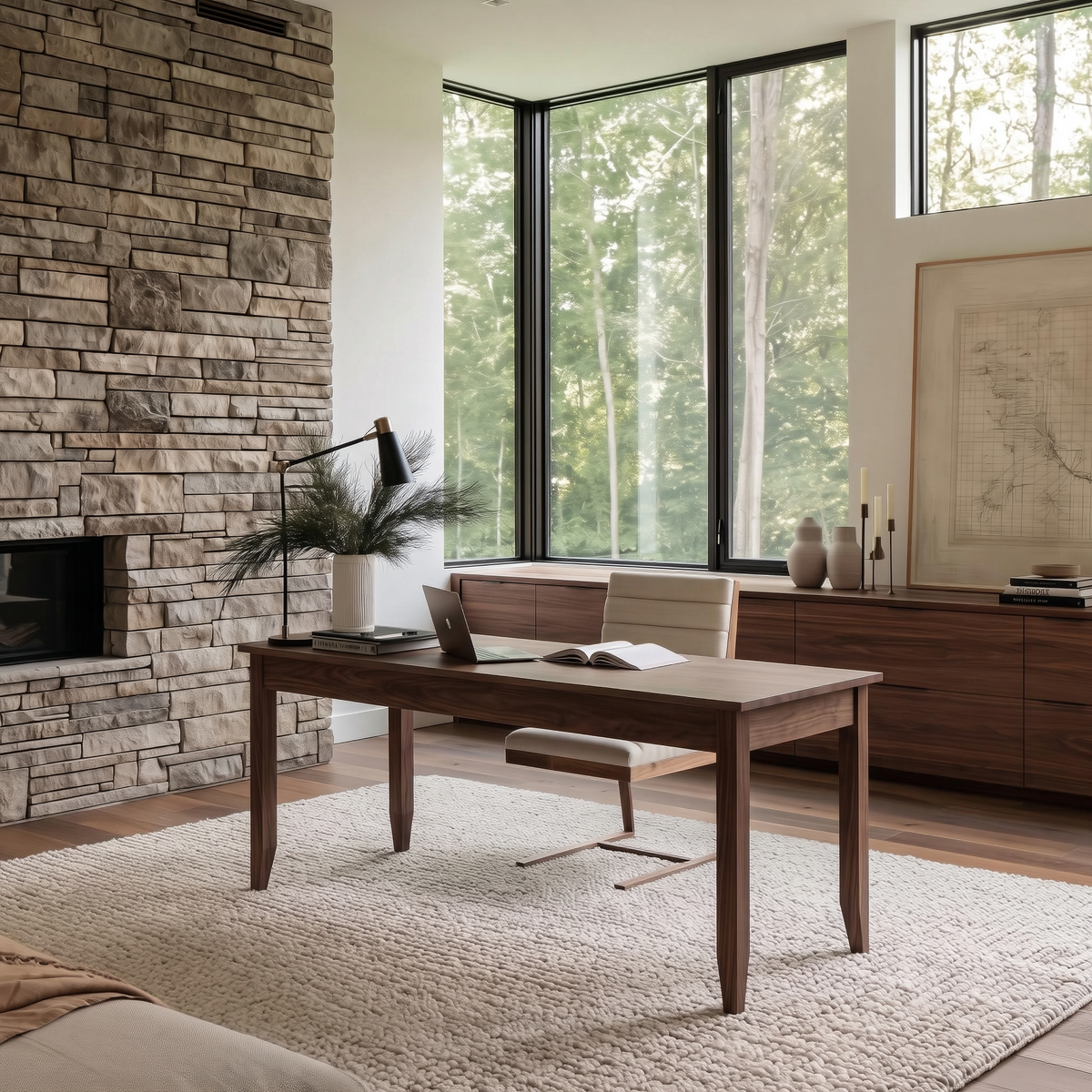 A mid-century modern wooden writing desk with a light beige upholstered seat and chrome metal legs, styled in a bright, contemporary home office with a stone fireplace and large windows.