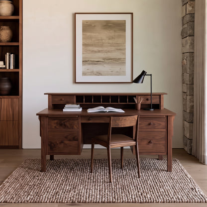 A mid-century modern wooden writing desk with a hutch and matching chair, styled in a warm, neutral-toned home office setting with a rug, shelving, and wall art.