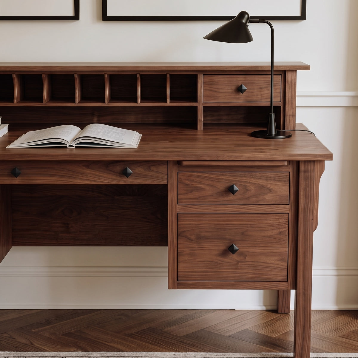 A dark walnut wood writing desk with a matching hutch featuring cubby shelves and drawers, styled with an open book and a black desk lamp in a home office setting.