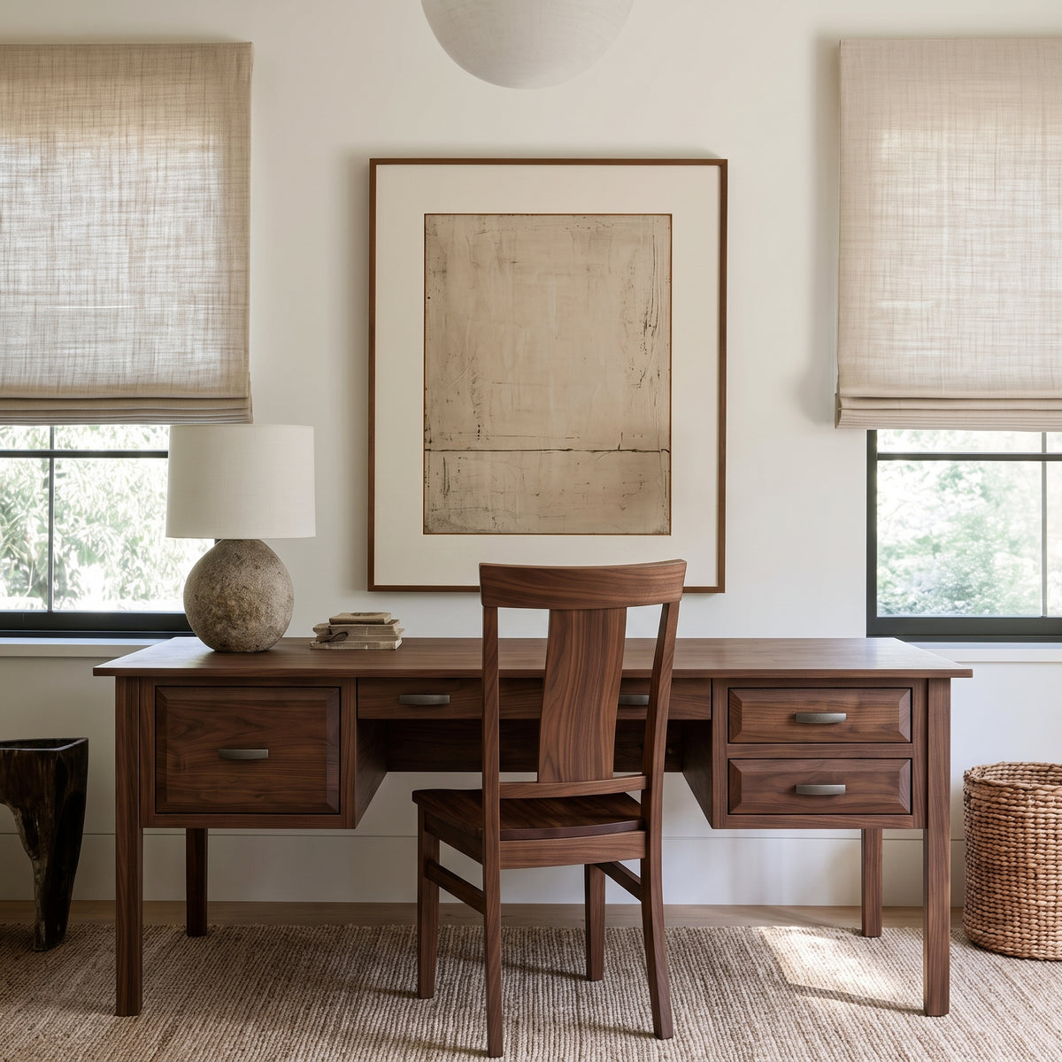 The Charlotte Hardwood Desk is a handcrafted solid hardwood desk with six drawers and a matching wooden chair centered in front of a wall with framed art and two windows.