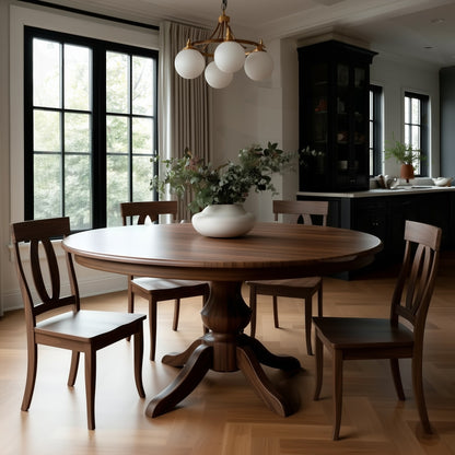 The Drayton Dining Table, handcrafted in the USA from solid walnut, is paired with four chairs and a white vase with greenery in a bright, modern dining room with large windows and elegant lighting.