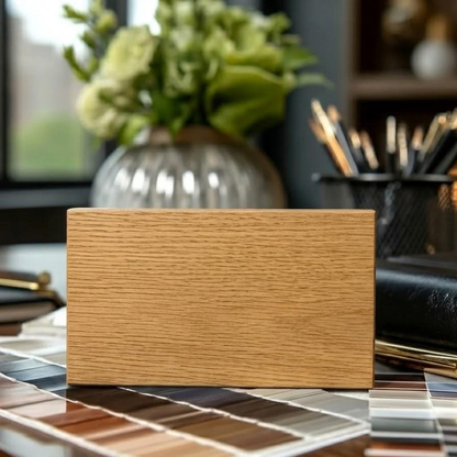 A Dining & Living Room Wood Sample rests on a table scattered with color swatches, while a vase of green flowers and a cup of pens appear softly blurred in the background, highlighting the diverse wood finish colors offered.
