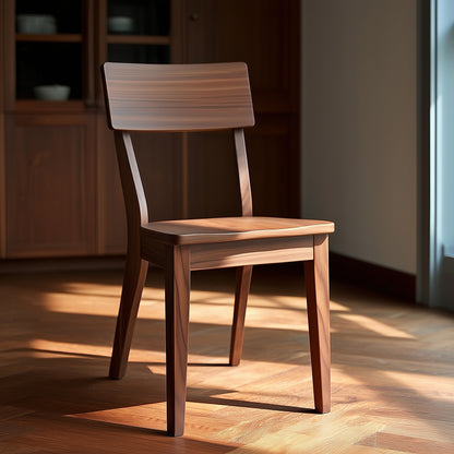 The Finnegan Chair, handcrafted in the USA from solid walnut with a simple design, sits on a sunlit wooden floor in a room featuring wooden cabinets and dishes in the background.