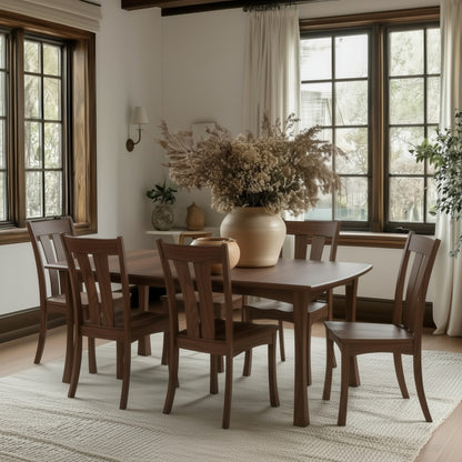 The Norwood Dining Table, handcrafted in the USA from solid walnut with extension leaves and six matching chairs, stands on a light rug. A beige vase with dried flowers sits at the center as sunlight filters through white curtains.