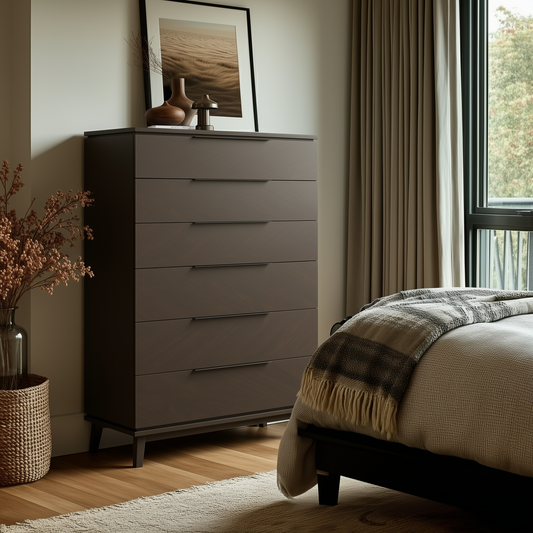 A modern bedroom features The Adelaide Chest of Drawers in dark wood, decorative vases, framed art, and a cozy bed with a plaid blanket. Natural light fills the room, highlighting a woven basket with dried plants on the wooden floor.