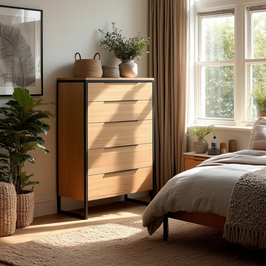 A sunlit bedroom features The Preston Chest of Drawers, potted plants, woven baskets, and a bed with neutral bedding. Light filters through a window with beige curtains, creating a calm and cozy atmosphere.