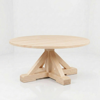Introducing the Vincent Round Coffee Table: A round, light wood table handcrafted in the USA, featuring a thick pedestal base with four angled supports and a durable finish to ensure lasting beauty. This solid wood piece is beautifully showcased on a white background.